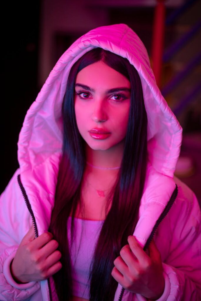 A striking portrait of a woman in a neon pink hoodie with vibrant lighting.